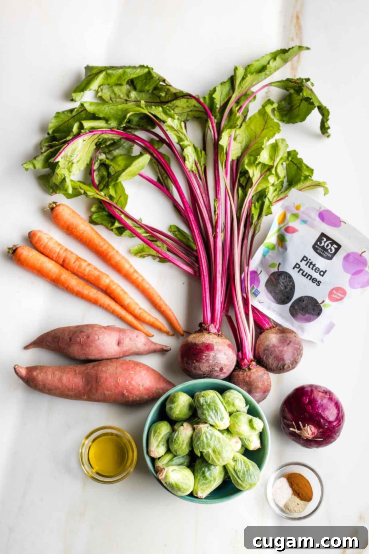 Selection of fresh ingredients for Tzimmes, including carrots, sweet potatoes, beets, red onion, Brussels sprouts, and prunes.