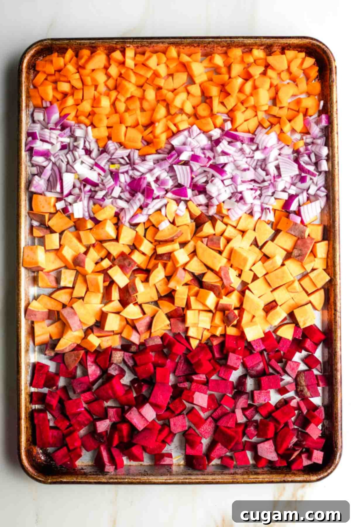 Chopped carrots, sweet potatoes, beets, and red onion on a baking sheet, drizzled with olive oil.
