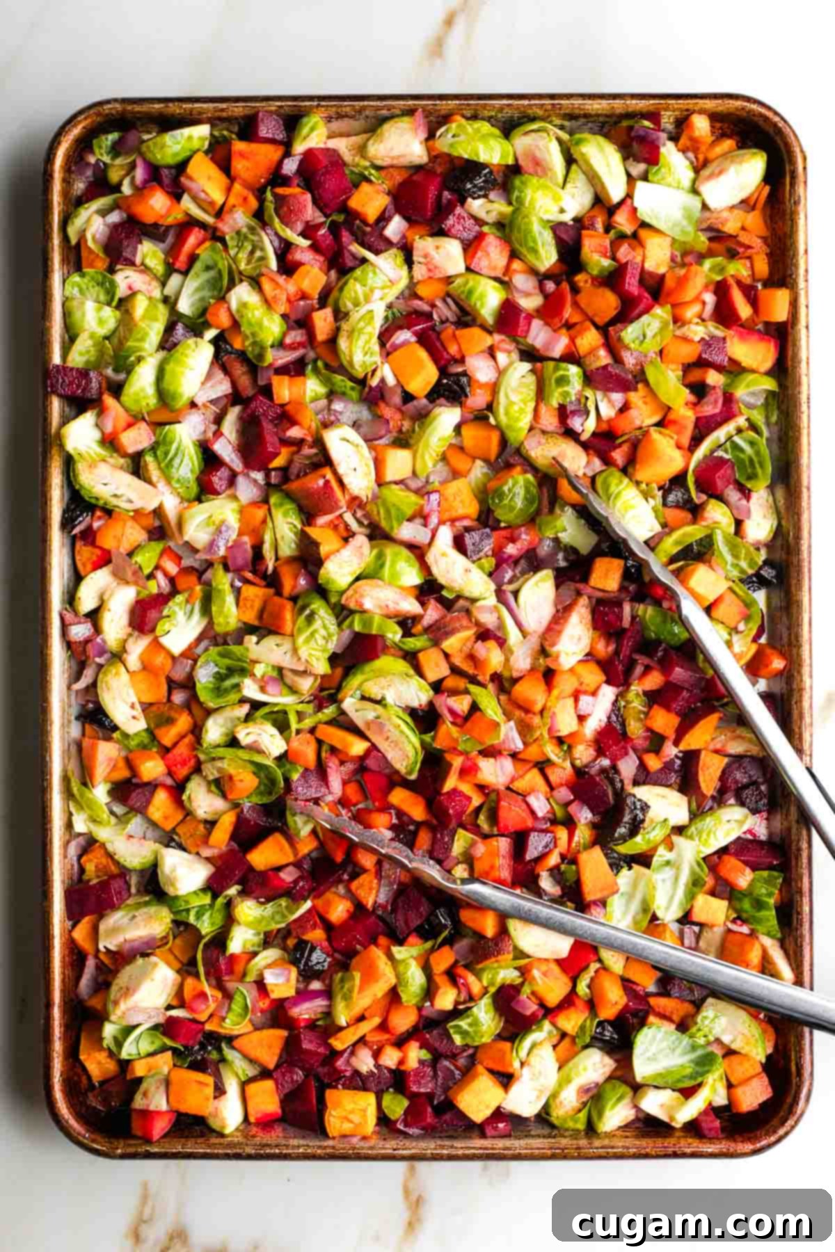 The roasted vegetables, Brussels sprouts, and prunes mixed together on the baking sheet, ready for further roasting.