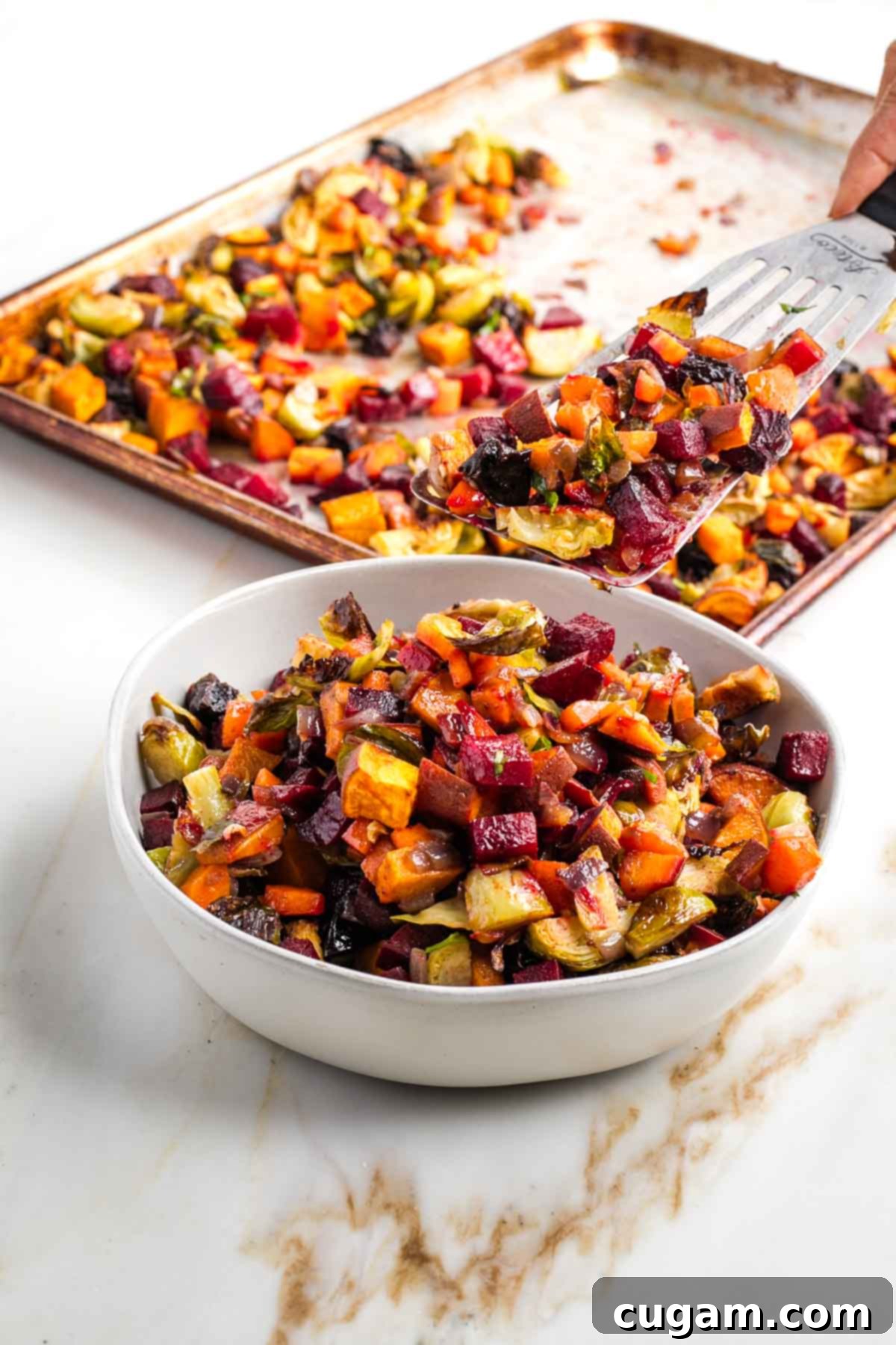 Spatula scooping tzimmes, roasted diced root vegetables, into a bowl. 