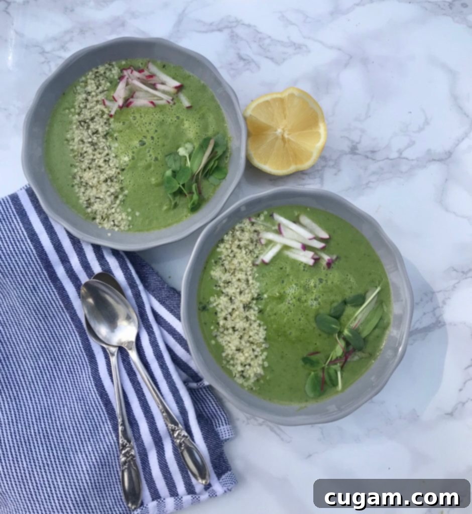 A bowl of bright green Spring Greens Soup, garnished with hemp seeds and fresh herbs, ready to be served.
