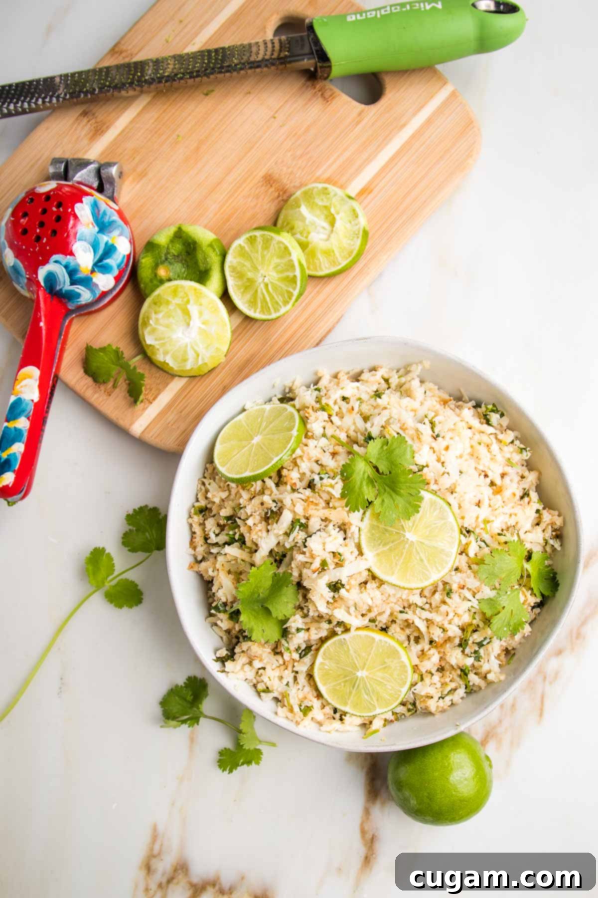 Effortless Stovetop Cauliflower Rice 11 Cauliflower Rice in a bowl with lime slices and cilantro. In the background is a cutting board with limes zested and squeezed.