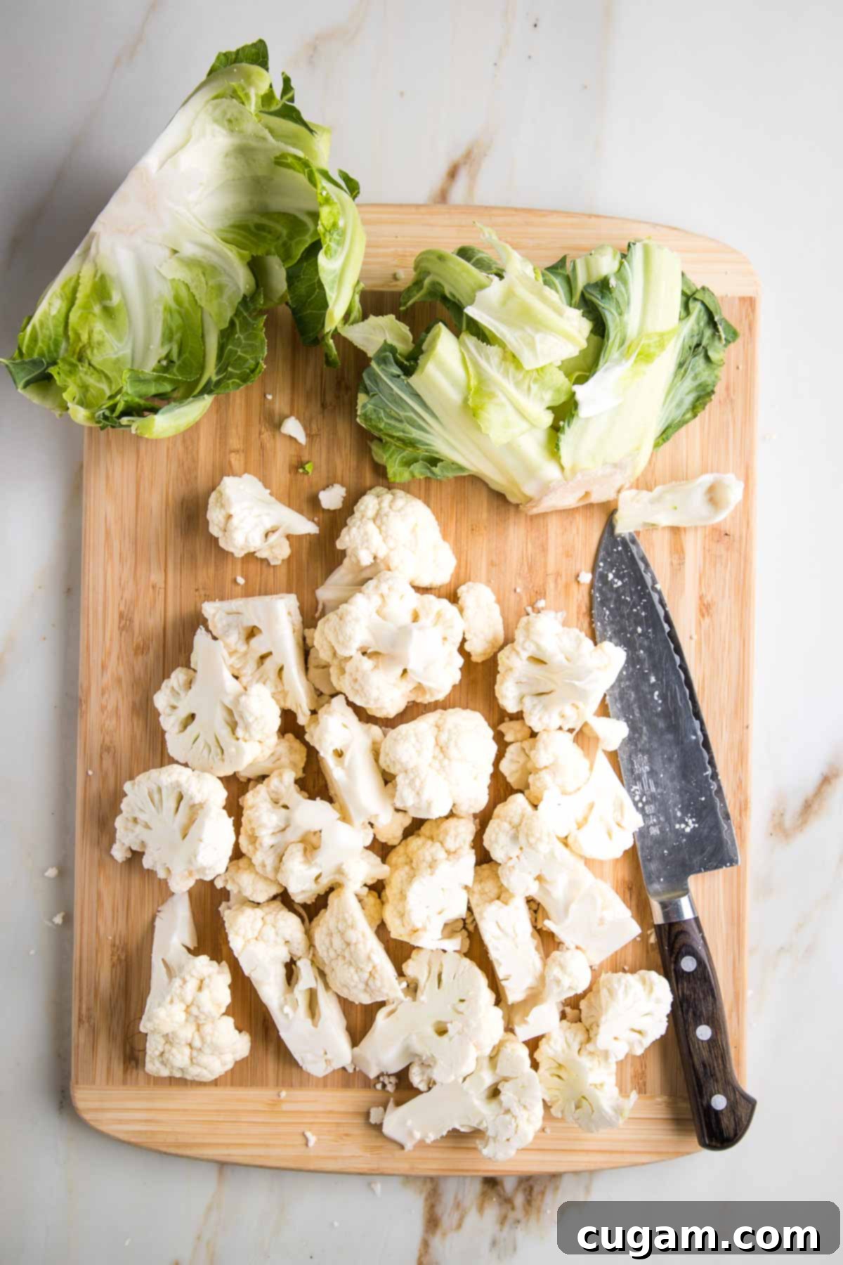 Effortless Stovetop Cauliflower Rice 5 Chopped cauliflower, showing the green outer leaves on the side of a cutting board.