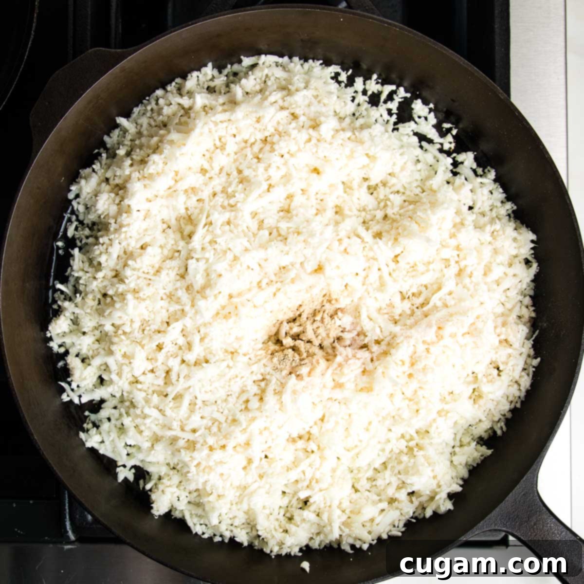 Effortless Stovetop Cauliflower Rice 7 Cauliflower rice in a cast iron skillet with sea salt and white pepper sprinkled into the center.