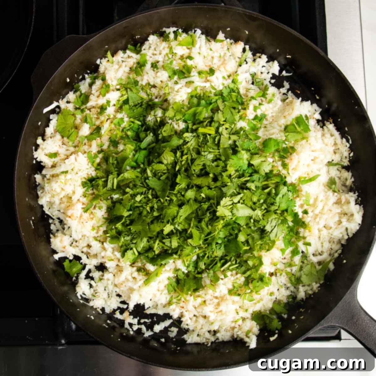 Effortless Stovetop Cauliflower Rice 8 Cast iron skillet with cauli-rice and a bunch of chopped cilantro on top.