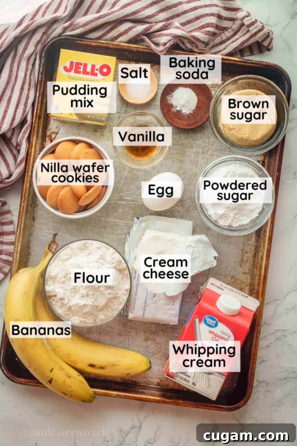 Ingredients for banana cream pie bars including brown sugar, instant pudding mix, cream cheese, heavy cream, vanilla, and fresh bananas, neatly arranged in glass dishes on a metal baking pan.