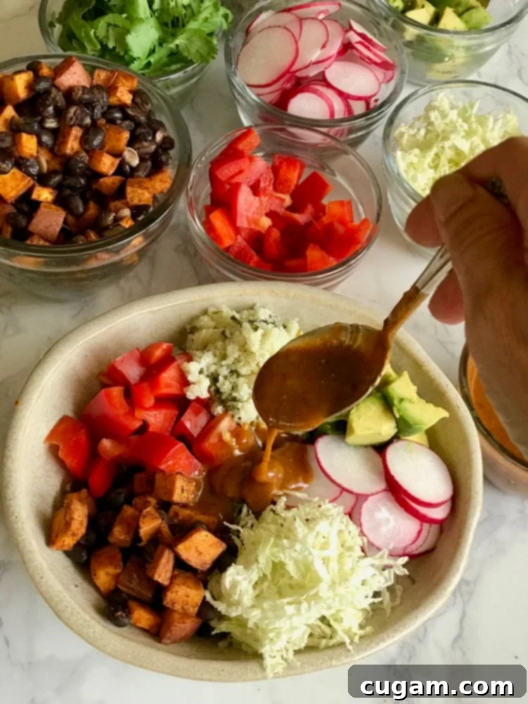 A hand carefully spooning rich, homemade red enchilada sauce over a colorful vegan bowl brimming with fresh and roasted vegetables, highlighting the vibrant ingredients.