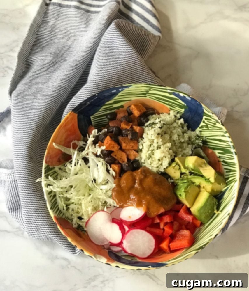 A beautifully assembled vegan enchilada bowl showcasing layers of fresh shredded cabbage, tender roasted sweet potatoes, fluffy cauliflower rice, creamy avocado, crisp radish, and vibrant red peppers, generously drizzled with rich, homemade enchilada sauce.
