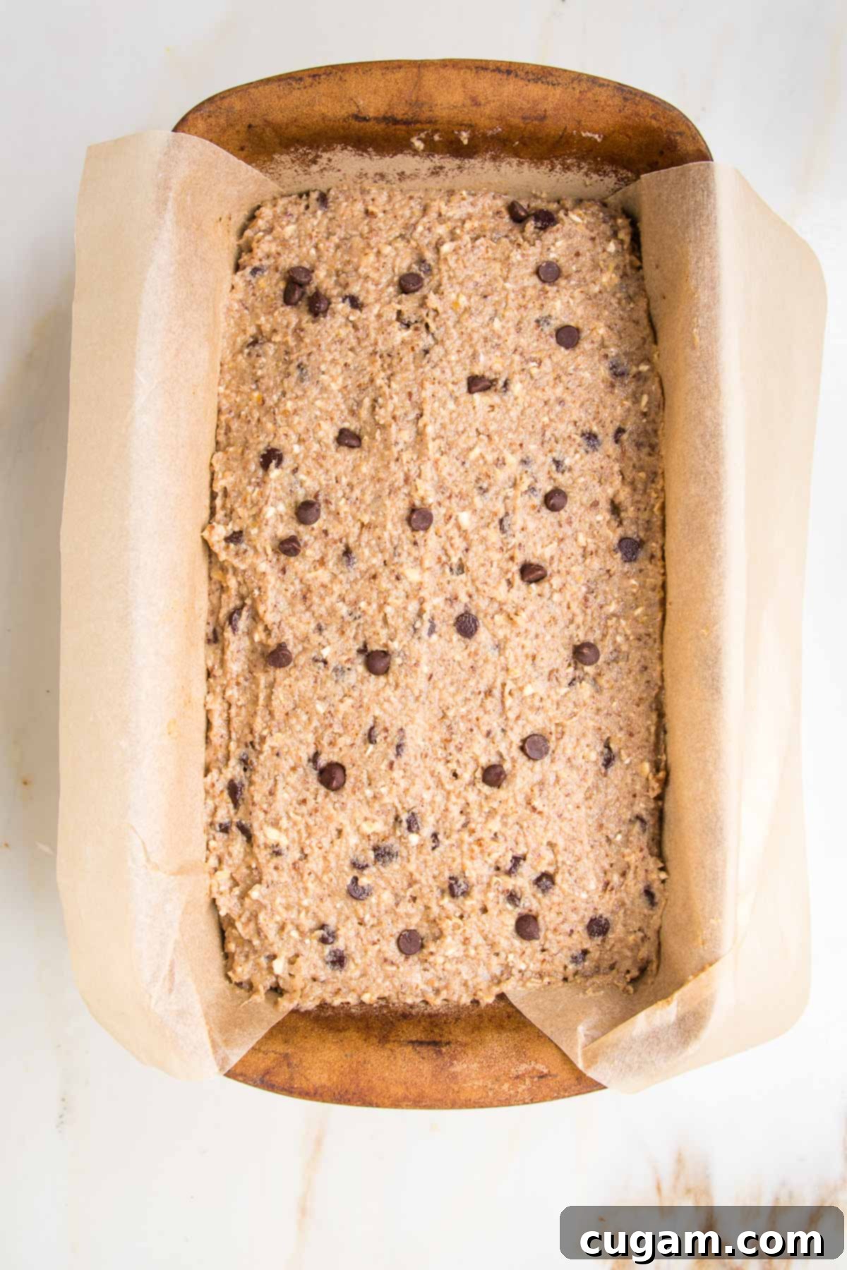 ceramic loaf pan, lined with parchment paper and filled with banana bread, sprinkled with chocolate chips