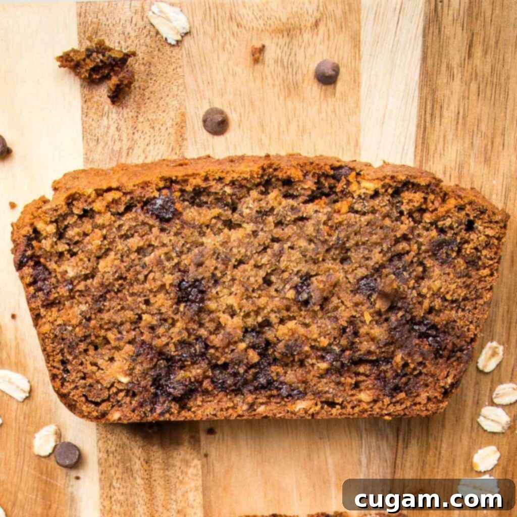 One slice of oatmeal banana bread on a wooden board with some crumbs of oats and chocolate chips