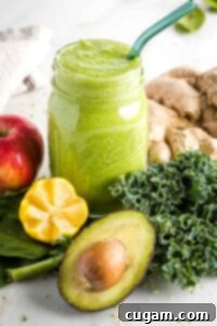 Green smoothie in a mason jar surrounded by greens, lemon, apple, ginger and avocado.