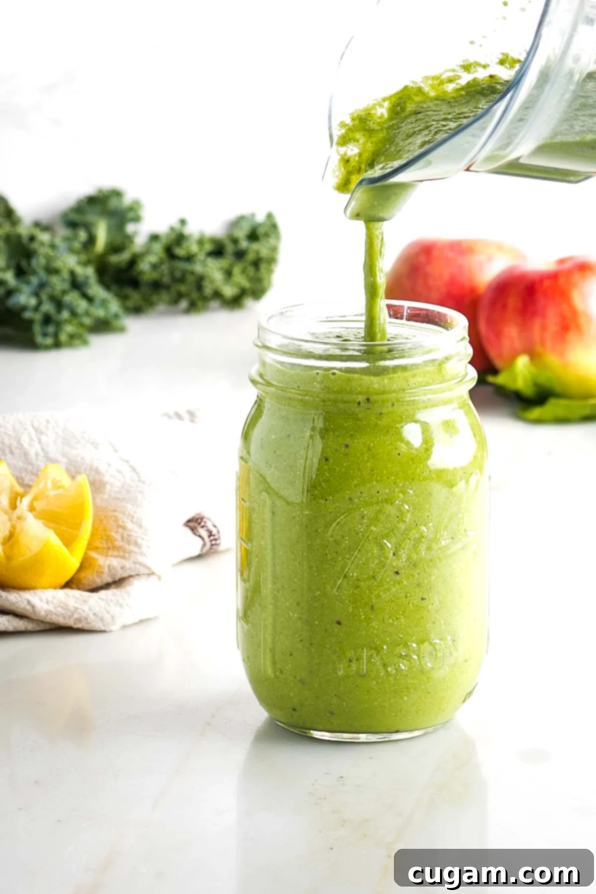 Pouring a green smoothie from a pitcher to a mason jar.
