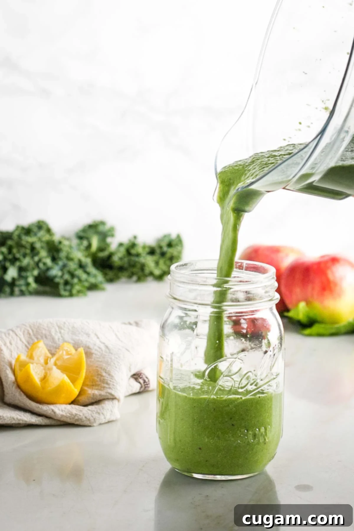 Pitcher of green smoothie, pouring into a wide mouth mason jar.