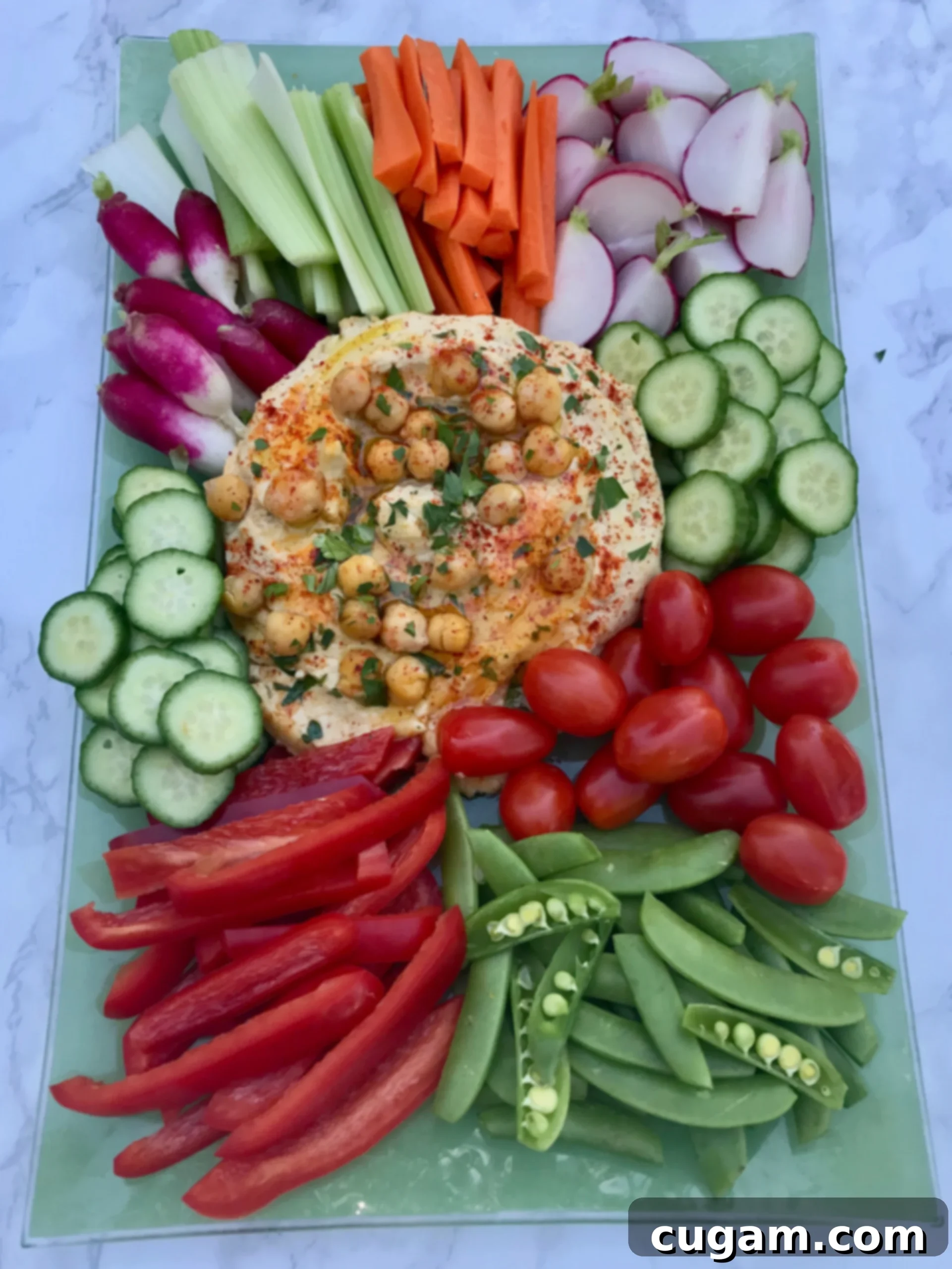 A large bowl of healthy hummus served with an array of fresh, colorful vegetables like carrots, cucumbers, bell peppers, and celery sticks for dipping.