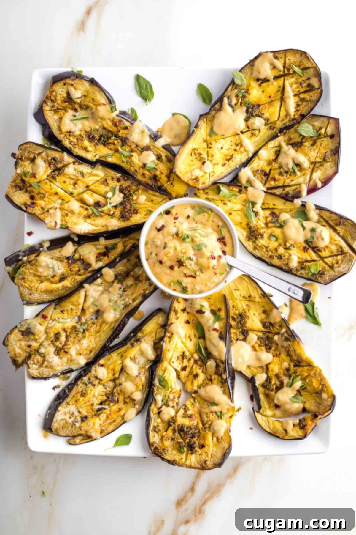 Platter filled with roasted eggplant slices with tahini, fresh herbs and crushed red pepper.