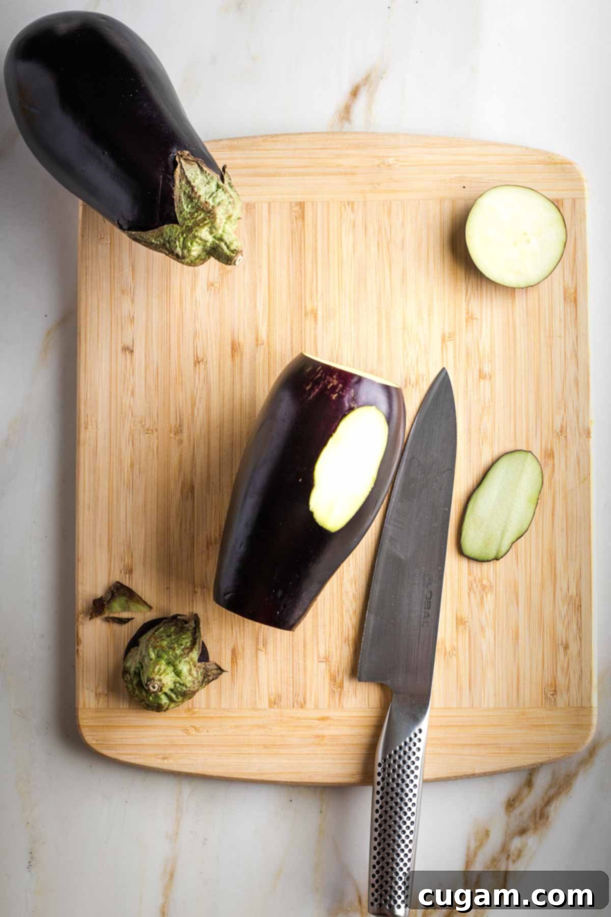 Trimming top, bottom and a sliver off the side of eggplant on a cutting board.