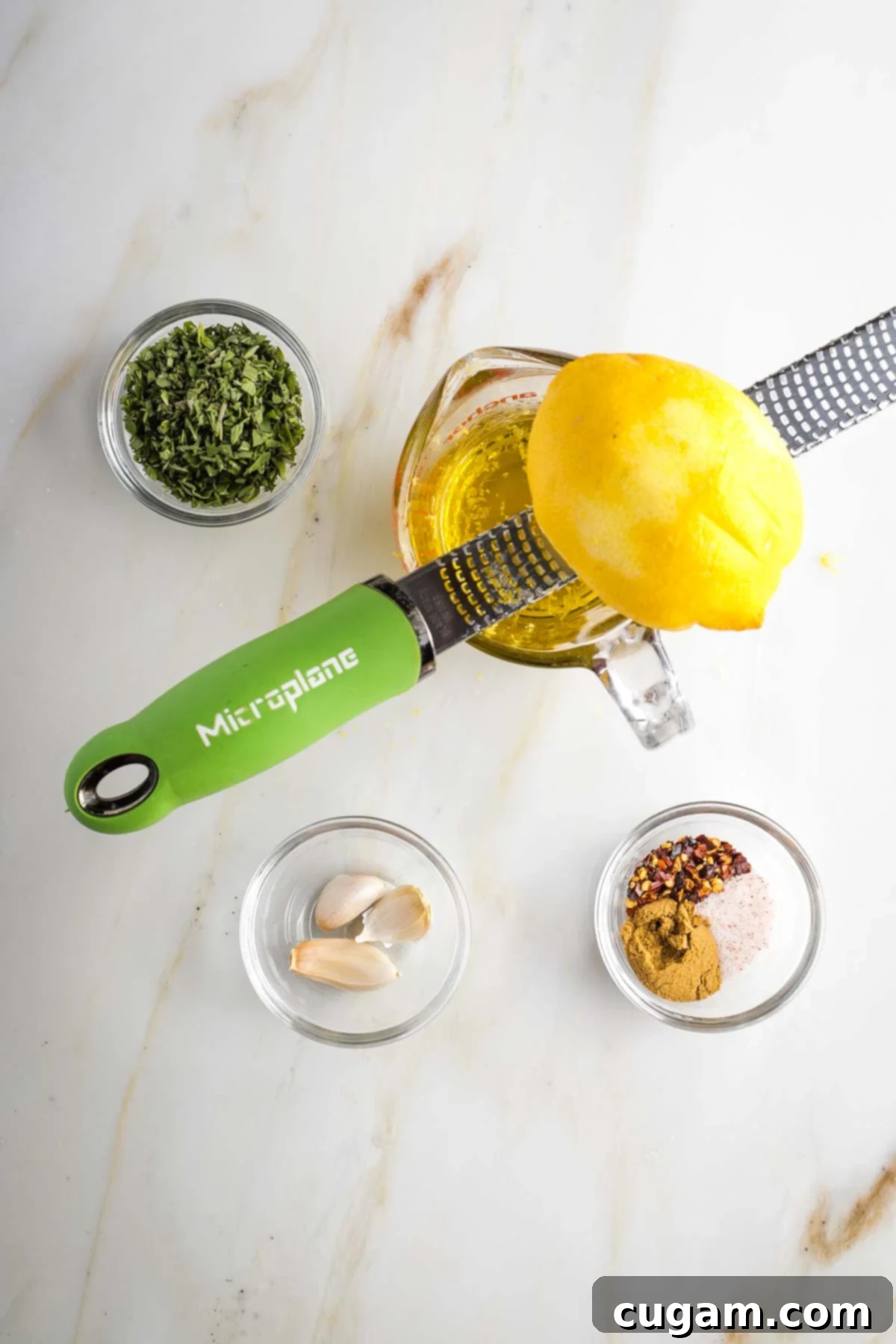 Zesting a lemon over some olive oil, plus small bowls with garlic, hebs and spices.