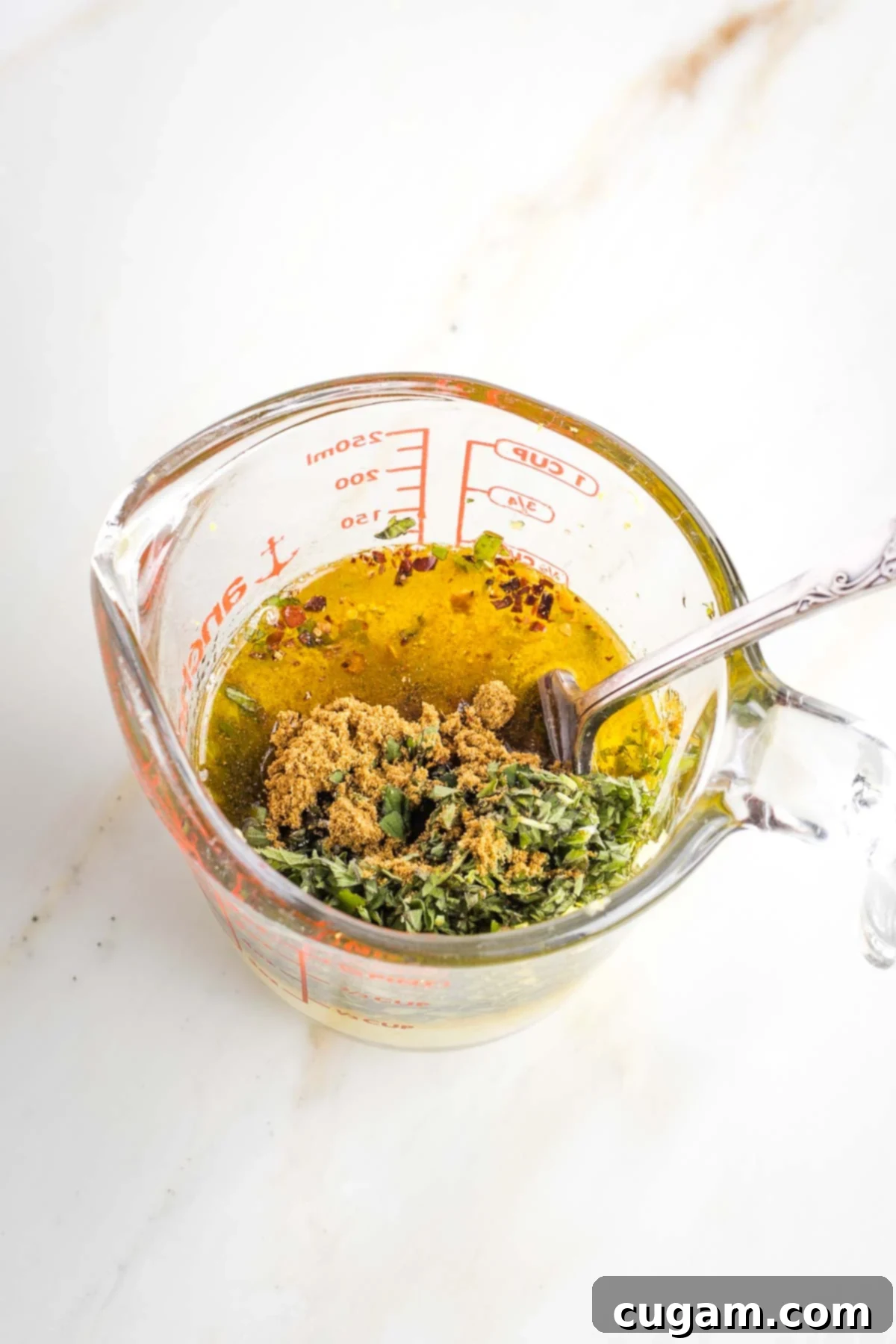 Measuring cup with lemon, oil, fresh herbs and spices.
