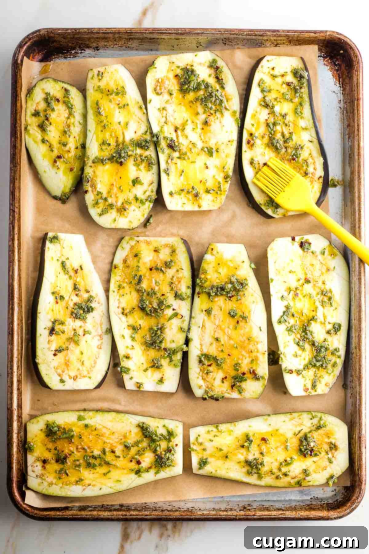 Baking tray with sliced eggplant being brushed with herby, lemon marinade.