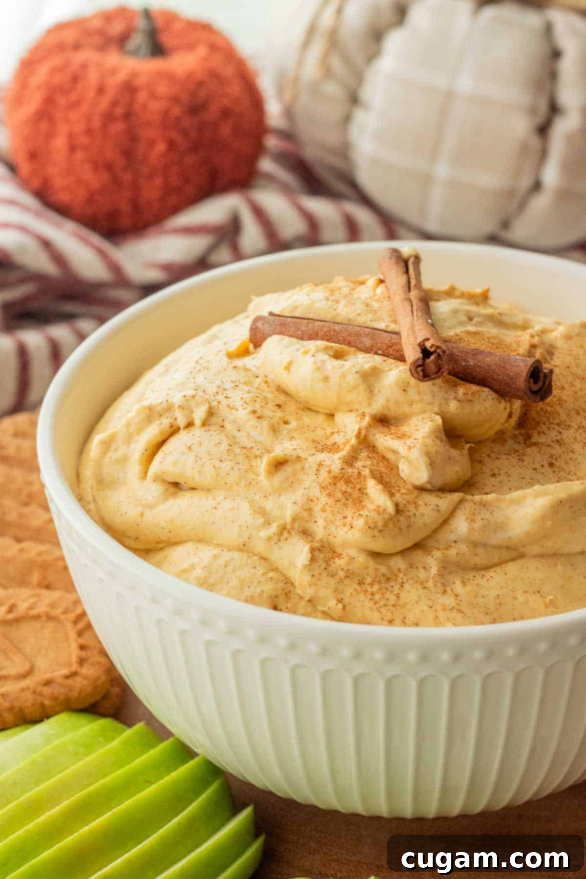 Irresistible Pumpkin Cream Cheese Dip 2 A beautifully whipped pumpkin cream cheese dip presented in a pristine white bowl, garnished with elegant cinnamon sticks, ready for a fall gathering.