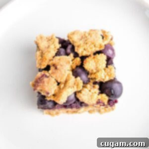 Close up of one blueberry crumble bar. You can see the jam and the fresh blueberries through the crispy top.