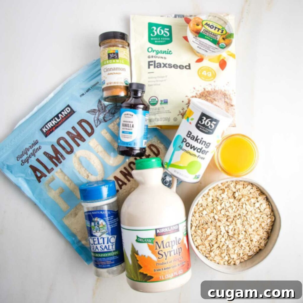 Ingredients for blueberry crumble bars: almond flour, oats, maple syrup, flax seeds, apple sauce, baking powder, vanilla, cinnamon and orange juice arranged on a white surface.
