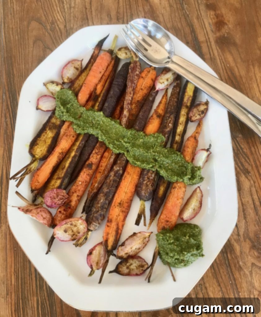 Close-up of golden-brown roasted vegetables served with a vibrant green dollop of carrot top pesto.
