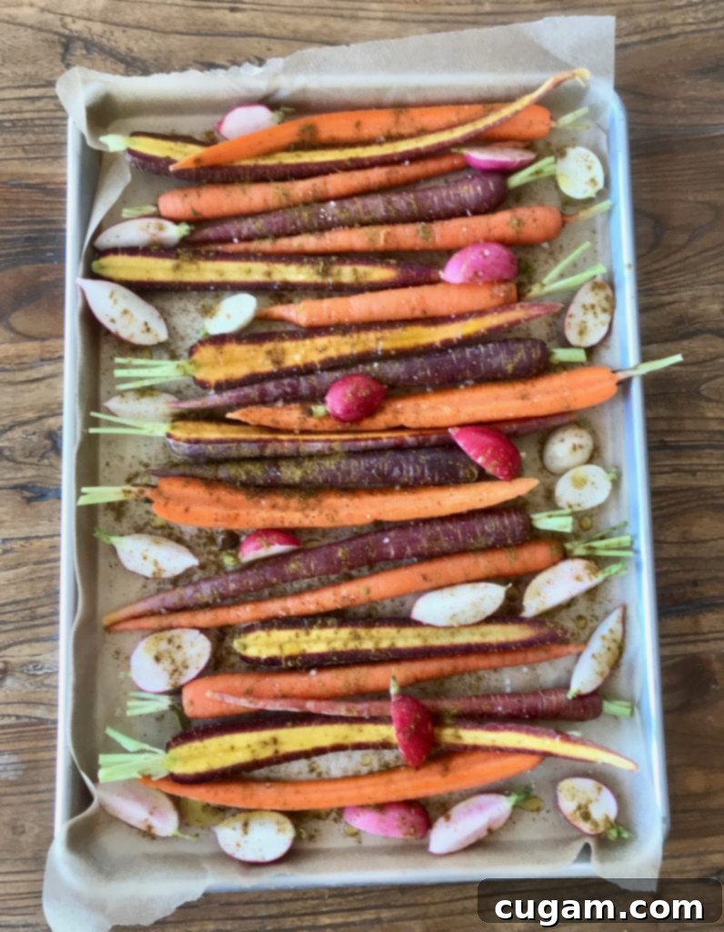A large baking sheet generously filled with sliced carrots and radishes, seasoned and ready for roasting until tender and caramelized.