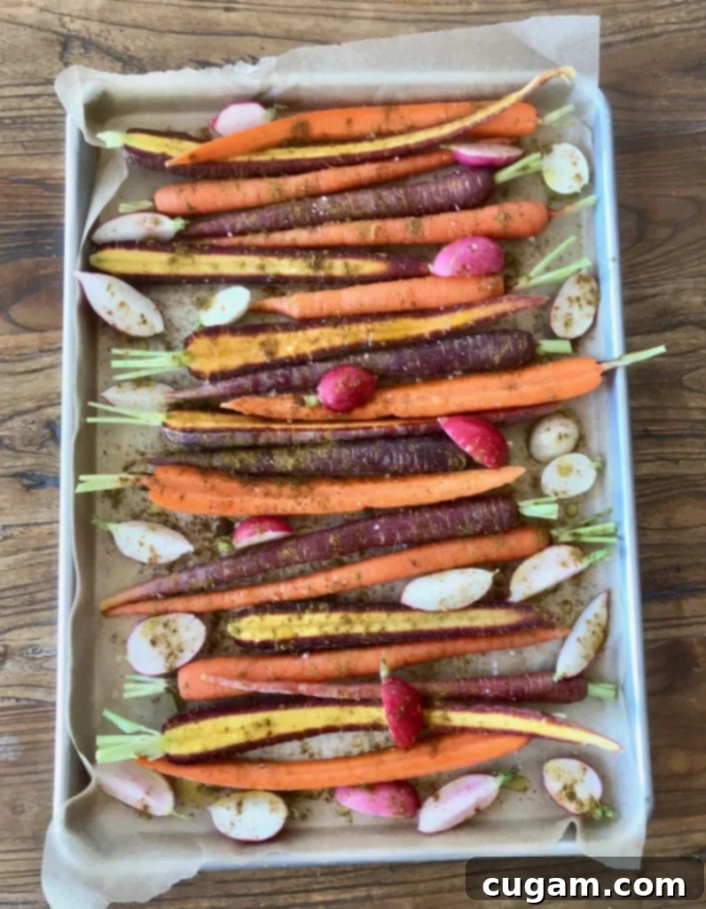 A baking sheet filled with an abundance of carrots and radishes, perfectly seasoned and ready for roasting.