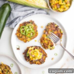 Zucchini Corn Fritters on a small white plate. One with sliced jalapenos, one plain and the other has mango salsa on top.