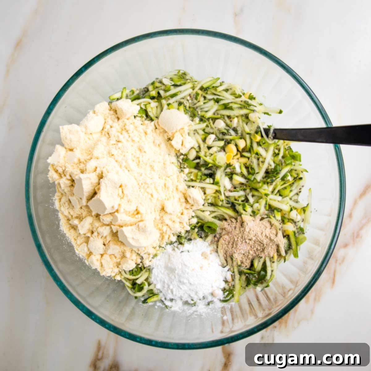 Mixture of wet ingredients for zucchini corn fritters, topped with dry ingredients like cornmeal, baking powder plus salt and pepper.