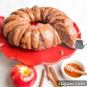 A beautifully baked Apple Cinnamon Bundt Cake on a red cake stand, generously drizzled with a rich chocolate sauce, ready to be served.