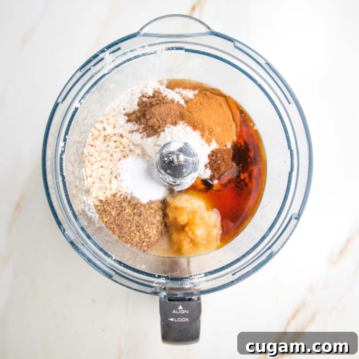 All the dry and wet ingredients, including flours, ground flaxseed, baking powder, and maple syrup, are gathered in the bowl of a food processor, ready for blending to create a wholesome apple cake batter.