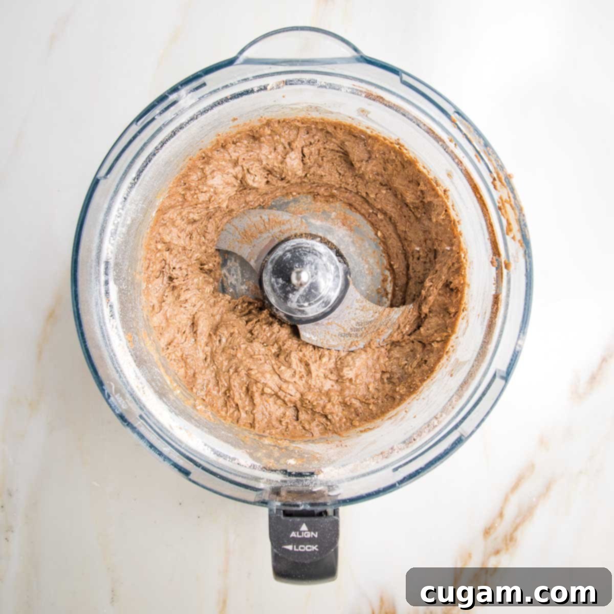 Smooth, thick cake batter in the bowl of a food processor, clearly showing the 's' blade that has efficiently blended all the ingredients into a creamy consistency.