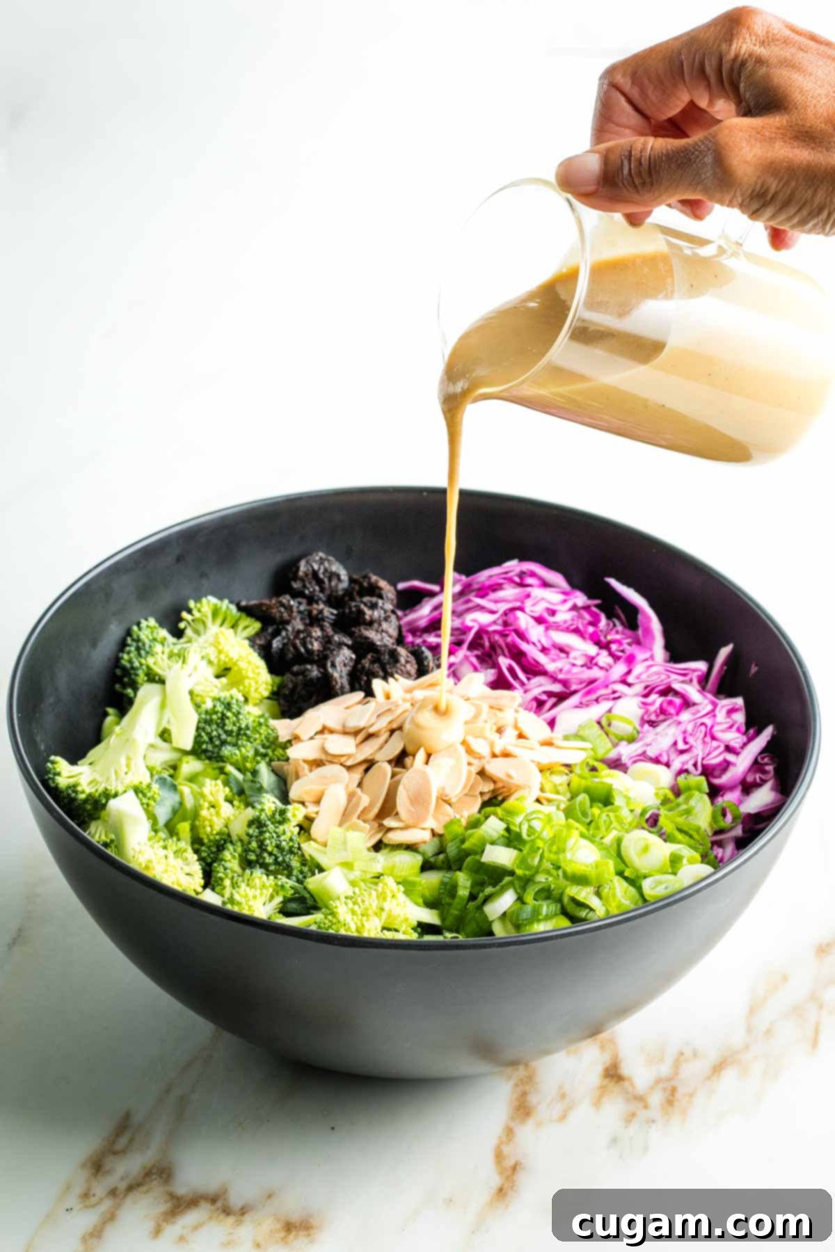 Crisp Raw Broccoli Salad with Miso Dressing 11 Pouring miso dressing over raw broccoli, cabbage, scallions plus almonds and dried cherries in a bowl.