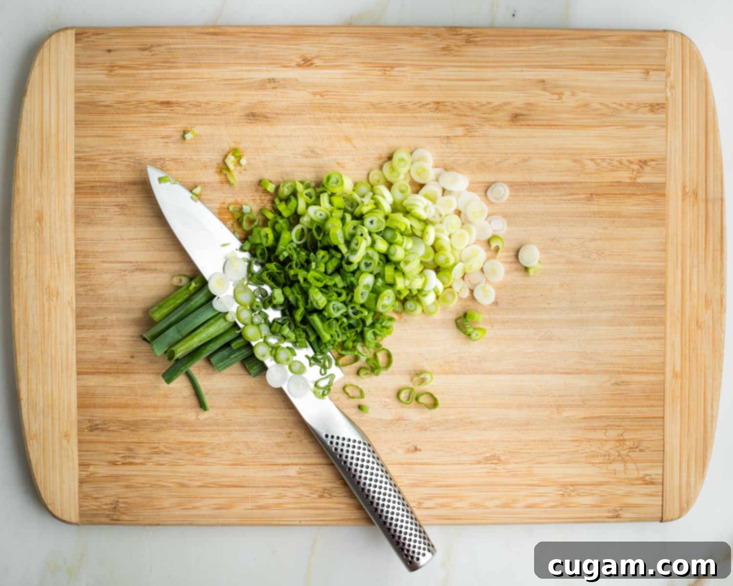 Crisp Raw Broccoli Salad with Miso Dressing 10 Thinly slicing white and green parts of green onions, on a wooden board.