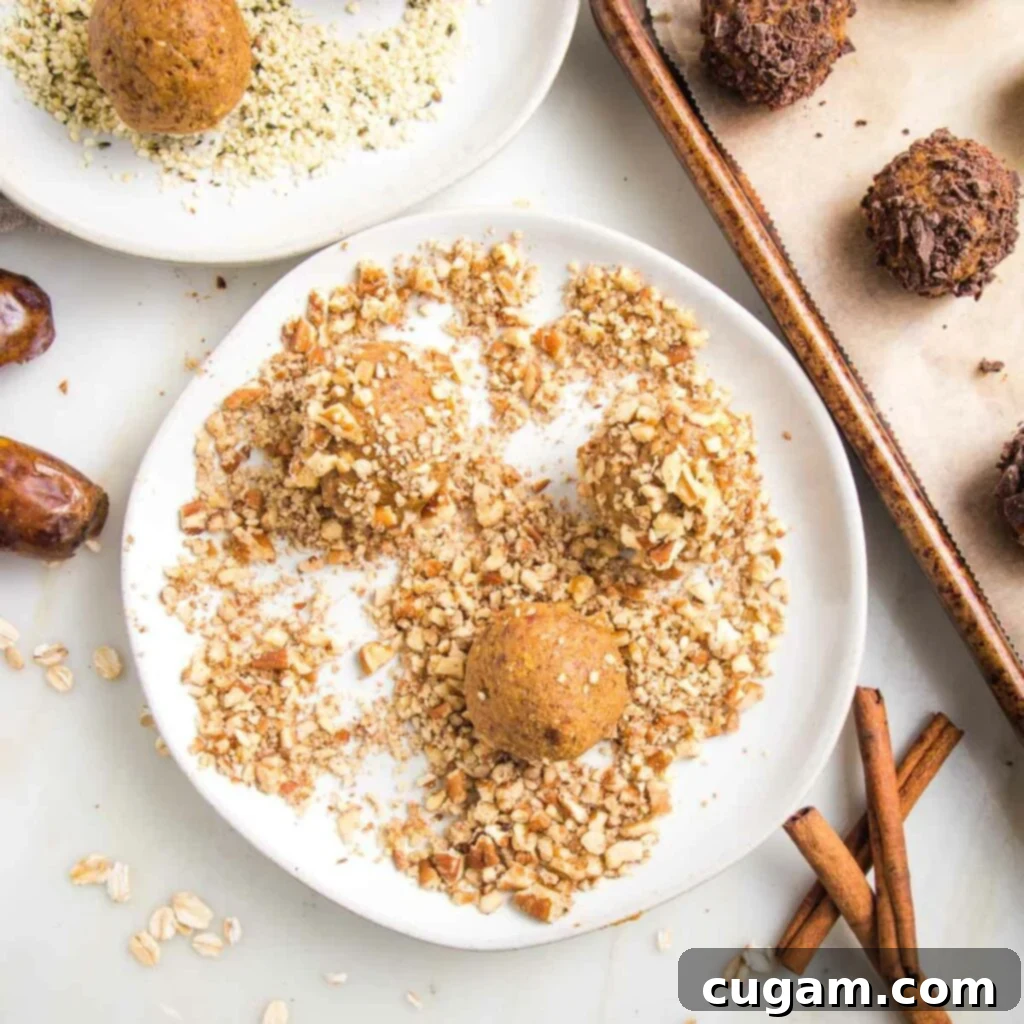 Small rimmed plate with crushed pecans and a three pumpkin balls rolling around to coat them in the nuts. There is a tray of pumpkin balls coated with chocolate and a glimpse of a plate with hemp seeds.