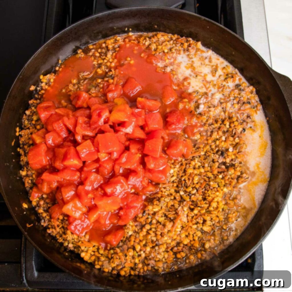 Diced tomatoes, almond milk, and tamari are added to a cast iron pot filled with sautéed veggies for vegan bolognese.