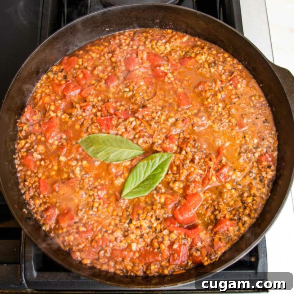 Chunky vegan bolognese, simmering in a cast iron skillet with bay leaves on top.