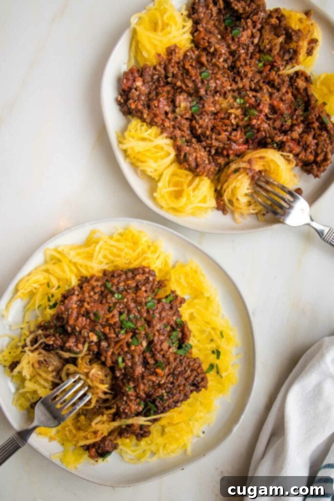 Two white rimmed plates filled with spaghetti squash and vegan bolognese.