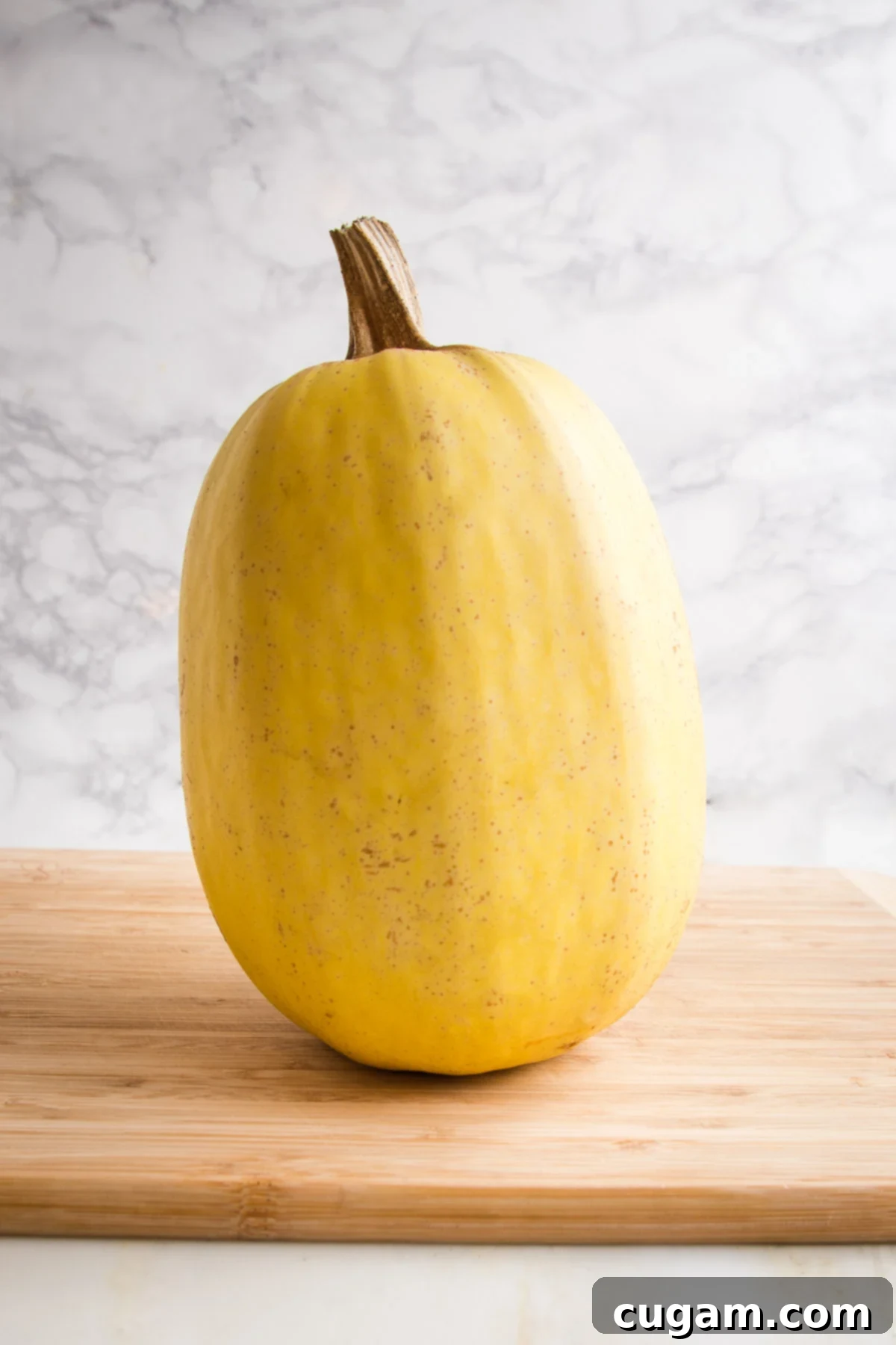 Whole spaghetti squash sitting on top of a wooden cutting board
