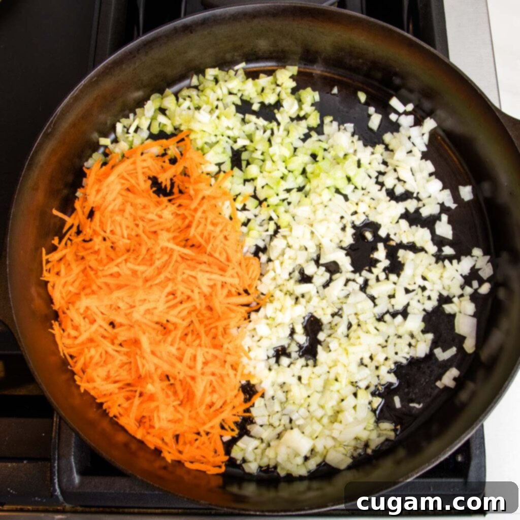 Cast iron skillet with diced onions, celery and shredded carrots sautéing.