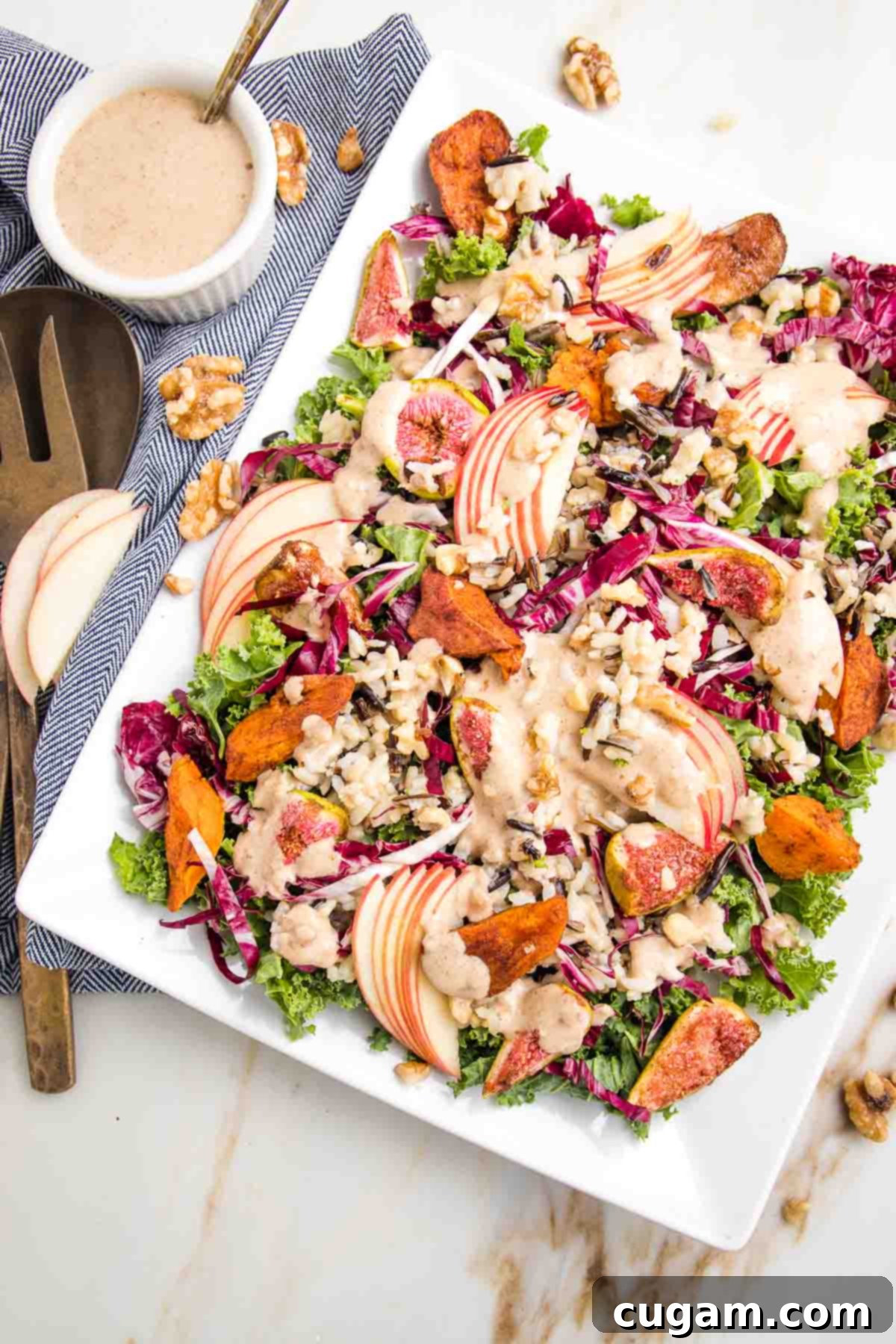 Platter of harvest salad showing greens, roasted sweet potatoes, figs and sliced apples with a creamy dressing.