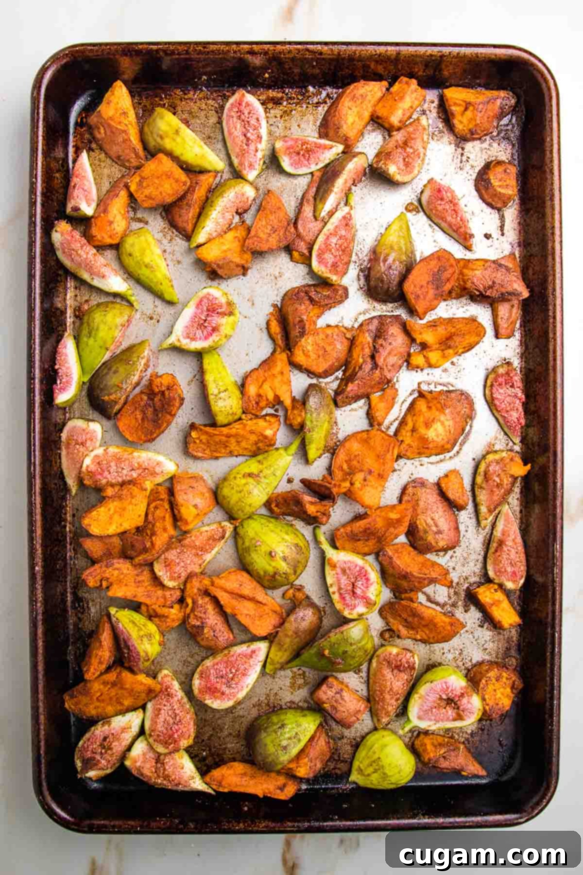 Rimmed sheet pan with roasted sweet potatoes and halved fresh figs. Roasted with cinnamon, cumin and sea salt.