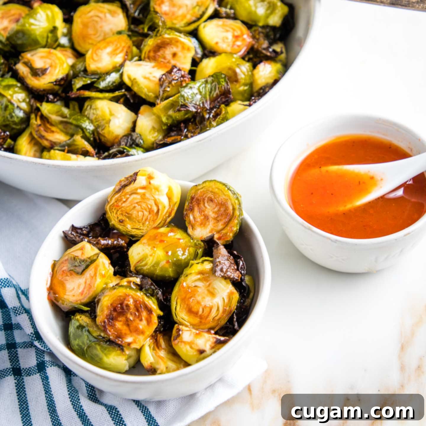 Serving bowl of crispy brussels sprouts, along with an individual bowl of sprouts drizzled with a sweet and spicy sauce and a small bowl with a spoon of extra honey-lime-sriracha sauce.