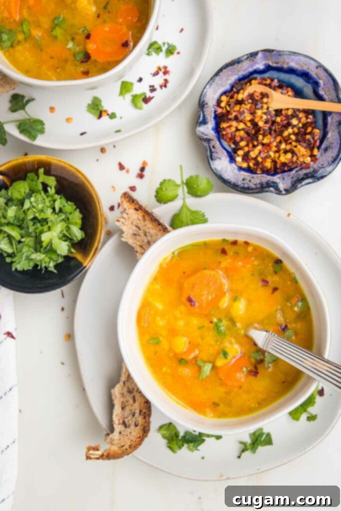 Bowl of yellow split pea soup with some crusty bread, fresh chopped parsley, crushed red pepper around the table. 