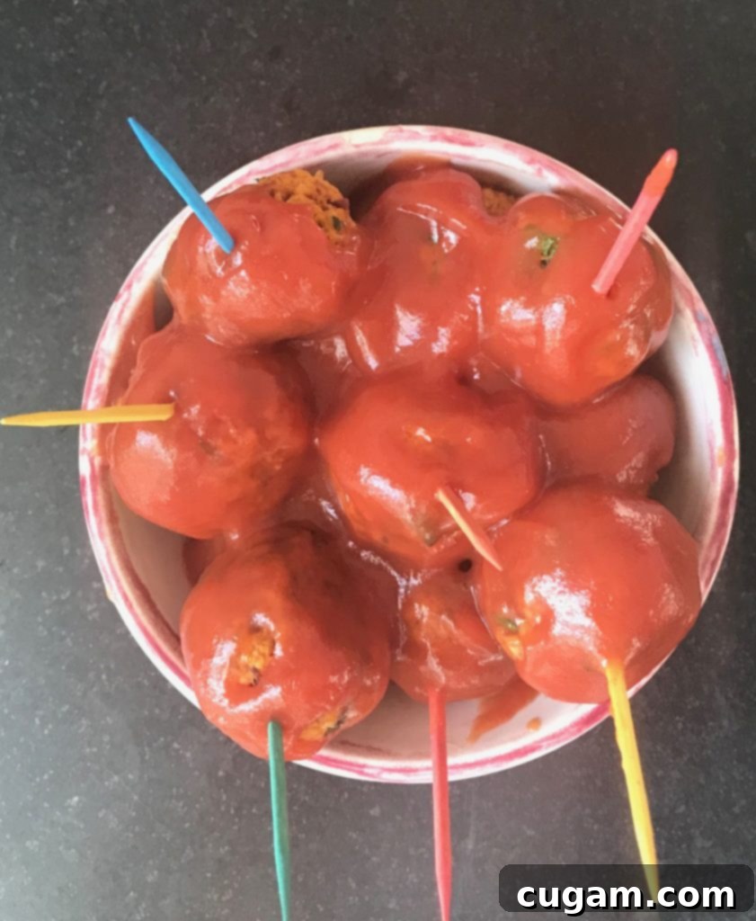 Small dish filled with vibrant red sweet and sour vegan meatballs, each pierced with a brightly colored toothpick, ready to be enjoyed as finger food.