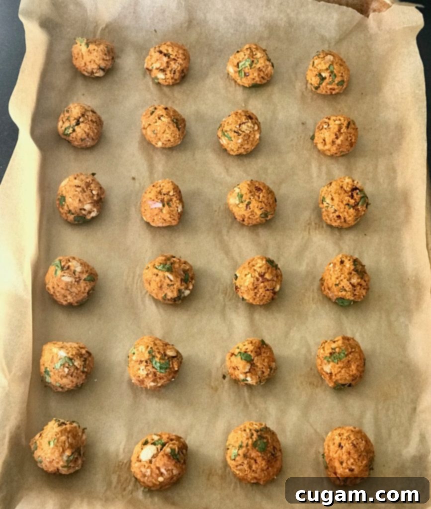Baked vegan meatballs arranged in neat rows on a parchment-lined baking tray, showcasing their perfect golden-brown finish.