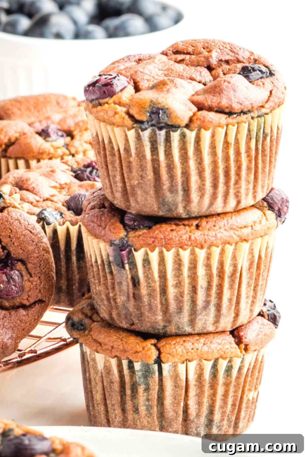 A stack of three perfectly golden-brown blueberry muffins, showcasing their fluffy texture and berry specks.