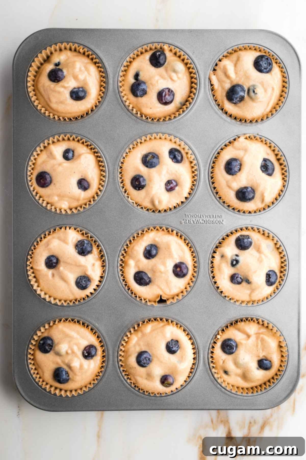 Blueberry muffin batter evenly scooped into a muffin tin lined with parchment wrappers.